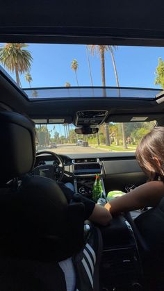 a young child sitting in the passenger seat of a car with palm trees behind him