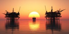 three oil rigs are silhouetted against the setting sun in an ocean with calm water