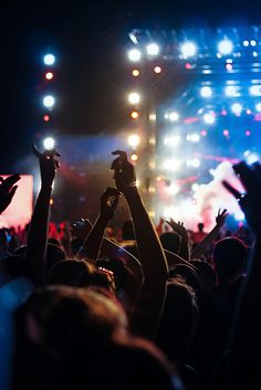 a crowd of people at a concert with their hands up in the air and lights on