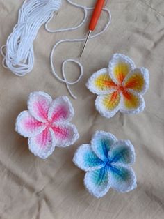 three crocheted flowers are sitting on a table with yarn and scissors next to them