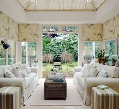 a living room filled with white furniture and lots of windows covered in shades of green