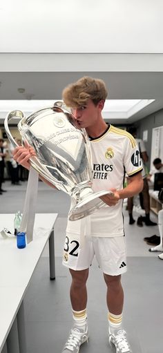 a young man holding a soccer trophy while wearing white and gold shorts, standing in front of a table