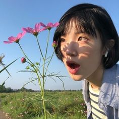 a young woman standing next to a pink flower on top of a lush green field