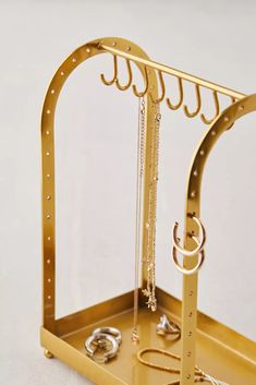 a gold jewelry holder with rings and chains hanging from it's sides on a white surface