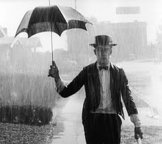 a man in a suit and hat holding an umbrella while walking down the street on a rainy day