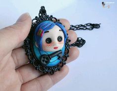 a hand holding a small necklace with a doll in it's center, on a white background