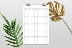 a calendar with a gold leaf next to it on a white surface, surrounded by greenery