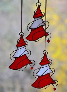 three red and white christmas bells hanging from strings in front of a window with trees