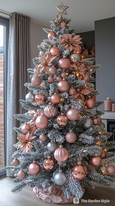 a decorated christmas tree with pink and silver ornaments in a living room next to a window