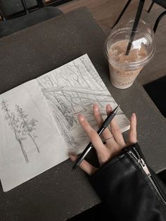 a person sitting at a table with a pen in their hand and drawing on paper