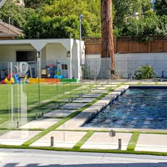 a backyard with artificial grass and pool in the back yard, fenced off by glass fencing