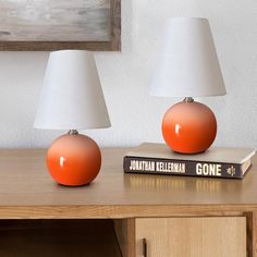 two orange and white lamps sitting on top of a wooden table next to a book