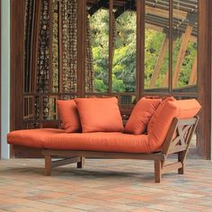 an orange couch sitting on top of a brick floor next to a wooden window sill