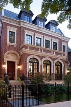 a large brick house with many windows and doors on it's front porch, next to a black fence