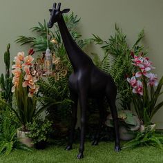 a statue of a giraffe standing in front of some plants and flowers with a chandelier behind it