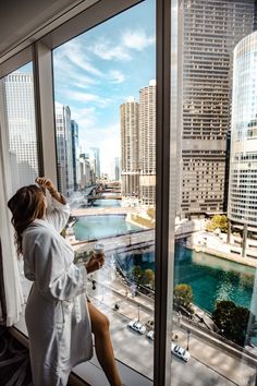 a woman in a bathrobe sitting on a window sill looking out at the city