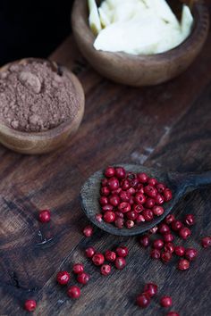 two wooden spoons filled with cranberries next to some powdered sugar on a table