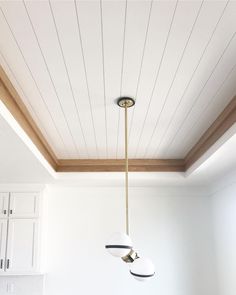 a kitchen with white walls and wooden ceilinging, two lights hanging from the ceiling