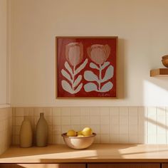 a bowl of lemons sits on a counter in front of a framed flower print