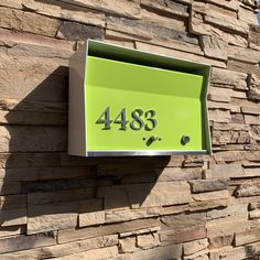 a green mailbox mounted to the side of a brick building with numbers on it