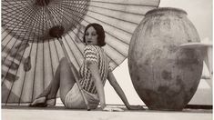 a woman sitting on the ground next to two large vases and an open umbrella