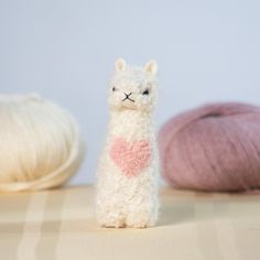 a white llama with a heart on its chest next to two balls of yarn