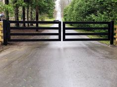 an open gate leading to a road in the woods