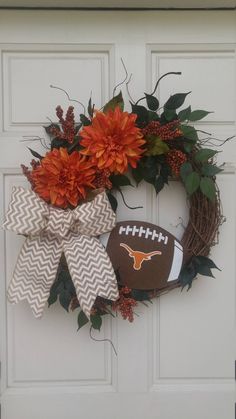 a wreath with a football on it and flowers in the middle is hanging from a door