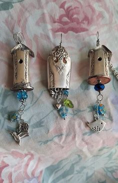 three birdhouses with charms hanging from them on a bed