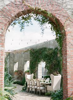 an outdoor dining area with white chairs and table surrounded by greenery on the wall