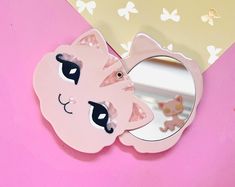 a pink cat shaped mirror sitting on top of a table next to a wallpaper