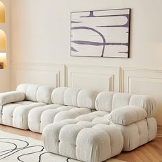 a large white couch sitting on top of a hard wood floor next to a painting