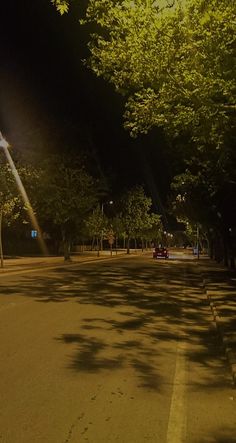 an empty street at night with trees lining the sides and people walking on the sidewalk