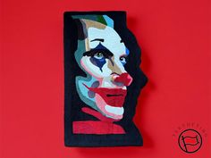 a piece of art that is on top of a red wall with the face of a clown