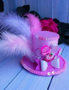 a pink hat with feathers and a cupcake in it on a blue wooden surface