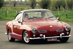 a red car driving down a road next to a lush green field