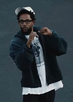 a man with glasses pointing to the side while wearing a hoodie and black sweatpants