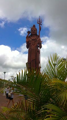 there is a large statue in the middle of some palm trees and people walking around