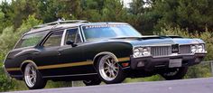 a black and gold station wagon parked on the side of a road with trees in the background