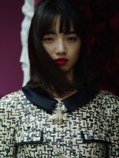 a woman with black hair and red lipstick standing in front of a purple wall wearing a patterned dress