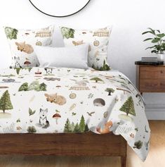 a bed covered in a white and green forest themed comforter set with woodland animals on it