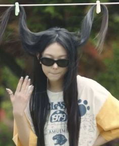 a woman with long black hair wearing sunglasses and an animal - themed shirt is waving at the camera