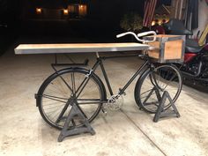 an old fashioned bicycle is parked in front of a van with a wooden table attached to it