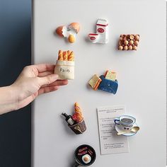 a person is holding a magnet with food on it and other items around the fridge