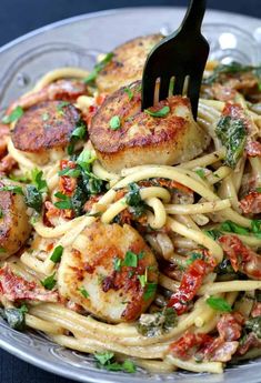 a fork is stuck into some pasta with scallops