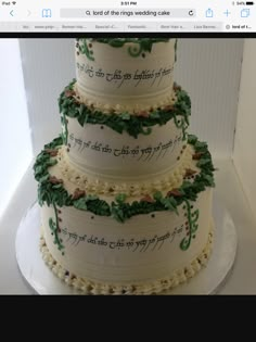 a three tiered cake decorated with green leaves and writing on the side, sitting on top of a white plate