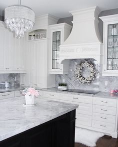 a large kitchen with white cabinets and marble counter tops, chandelier above the stove