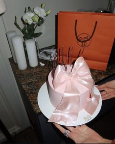 a woman is holding a cake with pink ribbon on it