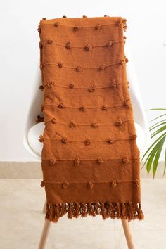 an orange blanket sitting on top of a white chair next to a potted plant