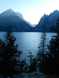 the mountains are covered in snow and some trees by the water's edge, as seen from across the lake